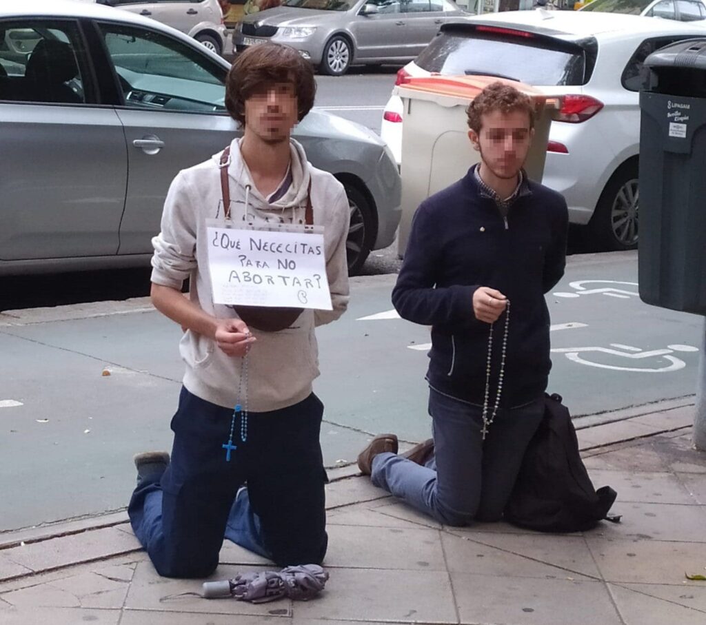 Dos jovenes de rodillas rezan frente a una clínica de interrupción del embarazo en Sevilla